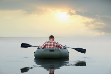 Photo of Man rowing inflatable rubber fishing boat on river, back view