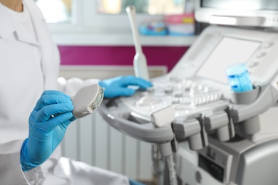 Photo of Sonographer holding ultrasound machine probe with gel in clinic, closeup. Space for text