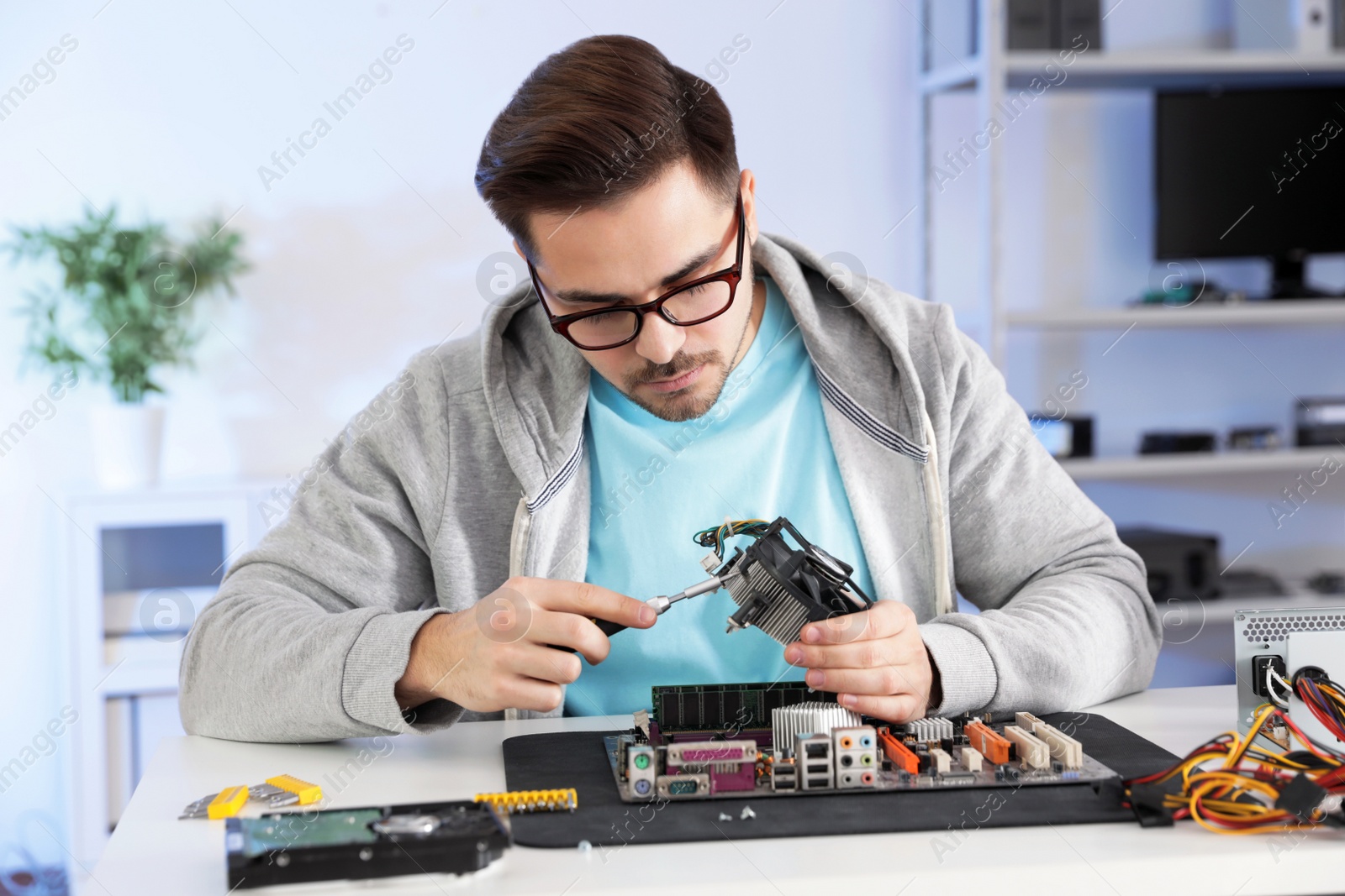 Photo of Male technician repairing motherboard at table indoors