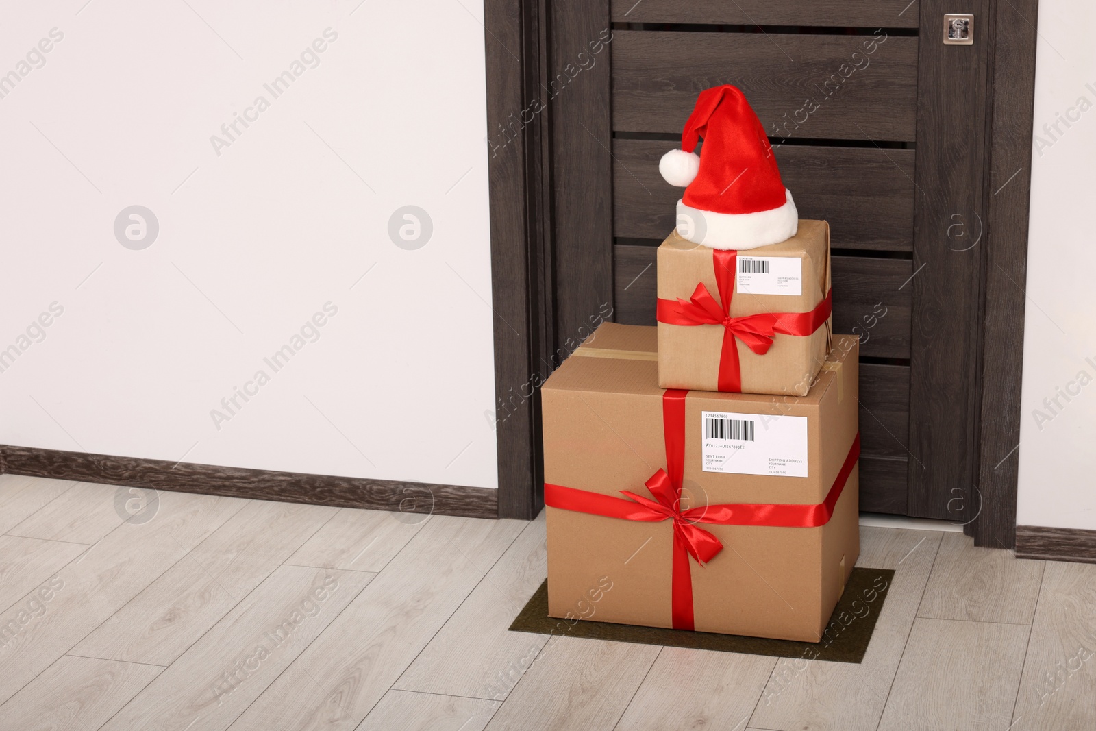 Photo of Christmas gift boxes and Santa hat near door indoors, space for text. Sending present by mail