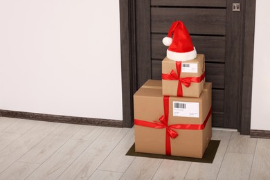 Photo of Christmas gift boxes and Santa hat near door indoors, space for text. Sending present by mail