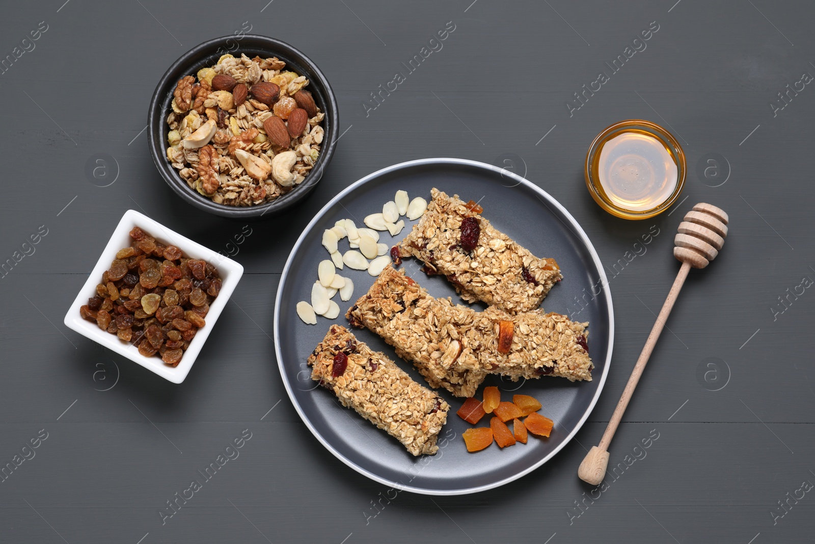 Photo of Tasty granola bars and ingredients on grey wooden table, flat lay