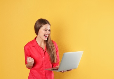 Emotional young woman with laptop celebrating victory on color background. Space for text