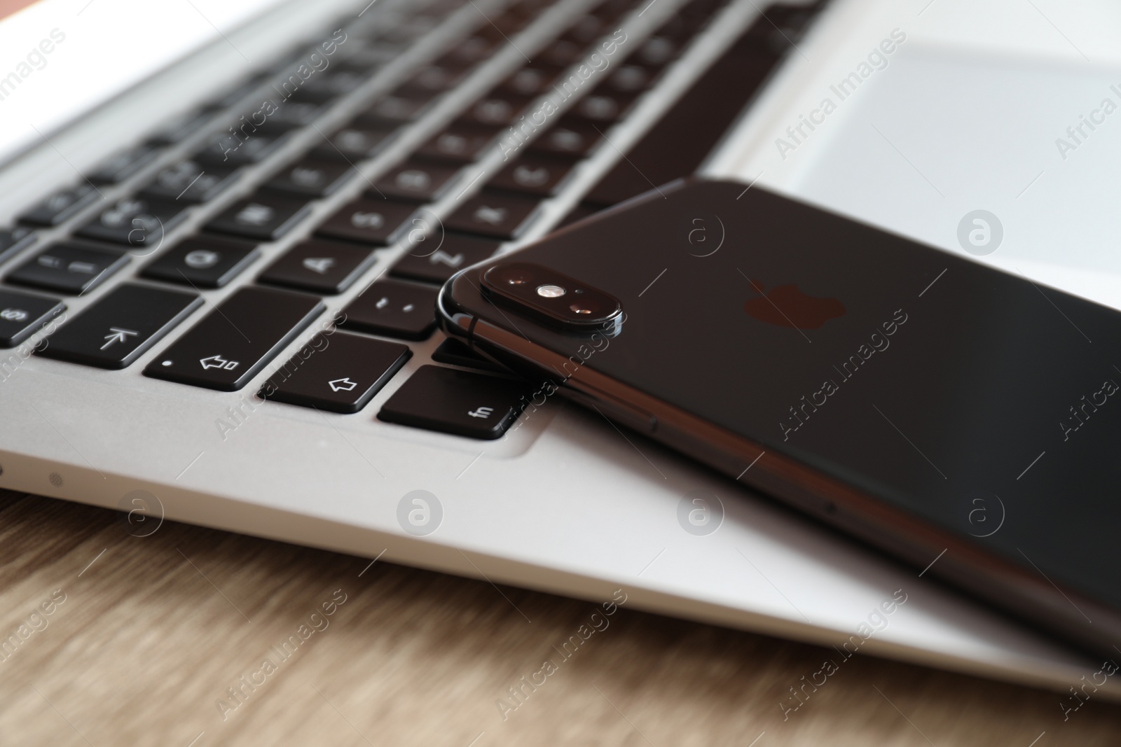 Photo of MYKOLAIV, UKRAINE - AUGUST 28, 2020: iPhone 11 and MacBook laptop on wooden table, closeup