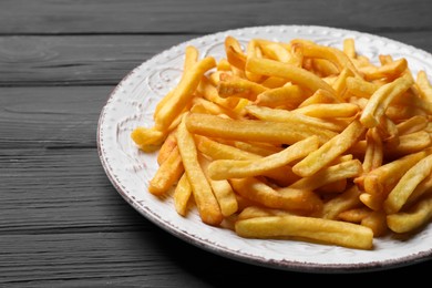 Photo of Plate of tasty french fries on black wooden table, closeup