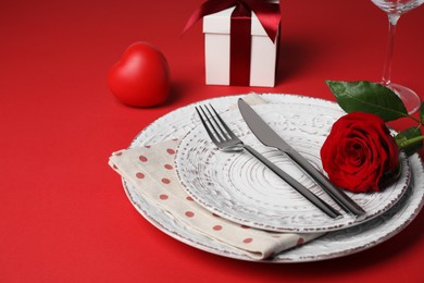Photo of Beautiful place setting with dishware, gift and rose for romantic dinner on red table