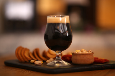 Glass of cold tasty dark beer served with snack on wooden table