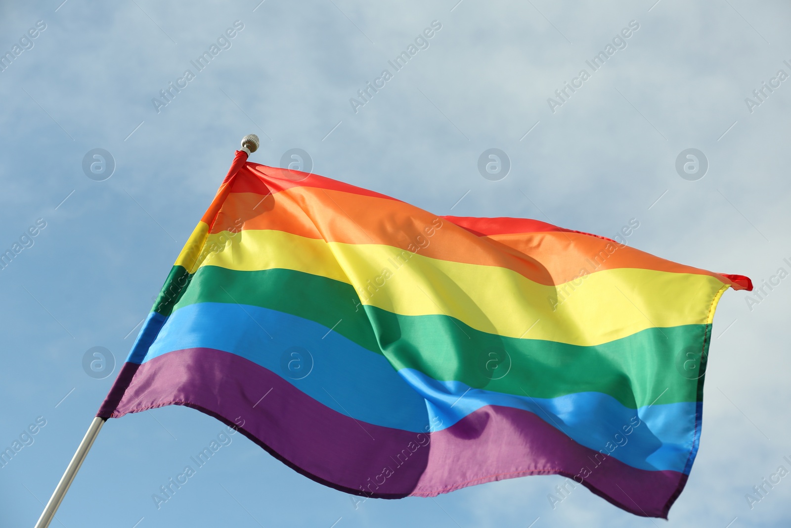 Photo of Bright rainbow gay flag fluttering against blue sky. LGBT community