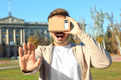 Photo of Young man using cardboard virtual reality headset outdoors