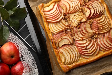 Photo of Baking tray with fresh apple galette, fruits and leaves on black table, flat lay