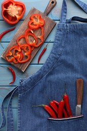 Flat lay composition with denim apron and fresh peppers on light blue wooden table