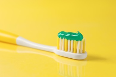 Brush with toothpaste on yellow background, closeup