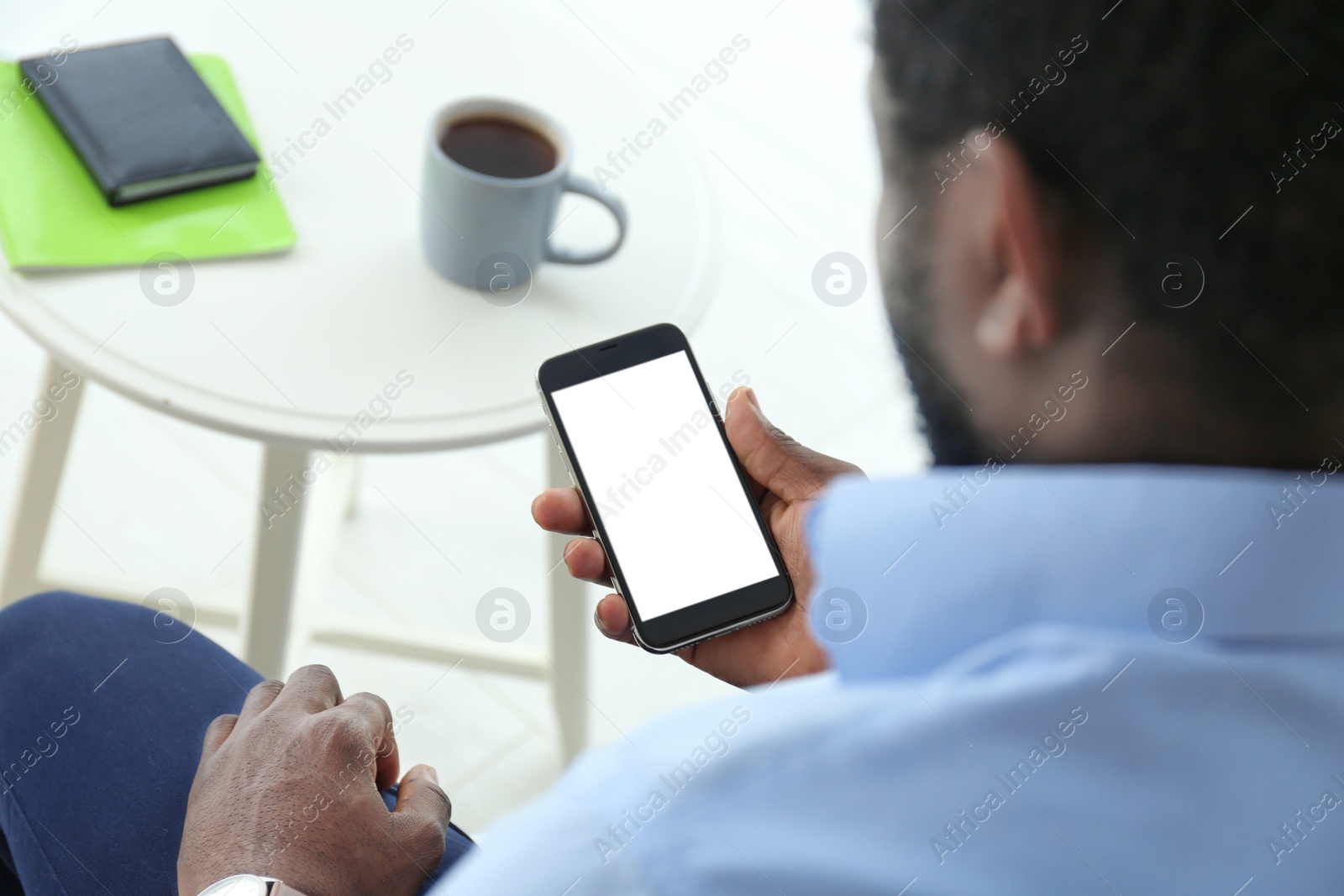 Photo of African-American man holding mobile phone with blank screen in hand indoors