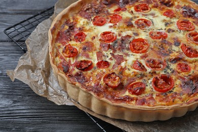 Photo of Delicious homemade quiche with prosciutto and tomatoes on black wooden table, closeup