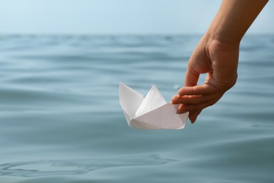 Photo of Woman holding white paper boat near sea, closeup. Space for text