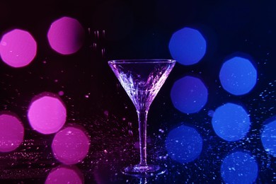 Photo of Martini glass and splashes in neon lights on dark background, bokeh effect