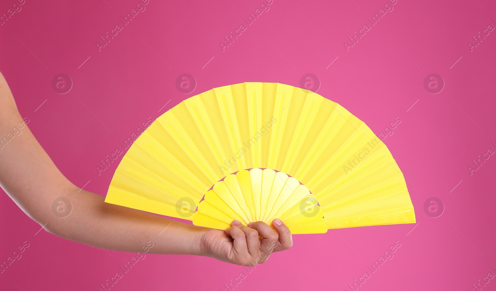 Photo of Woman holding yellow hand fan on pink background, closeup