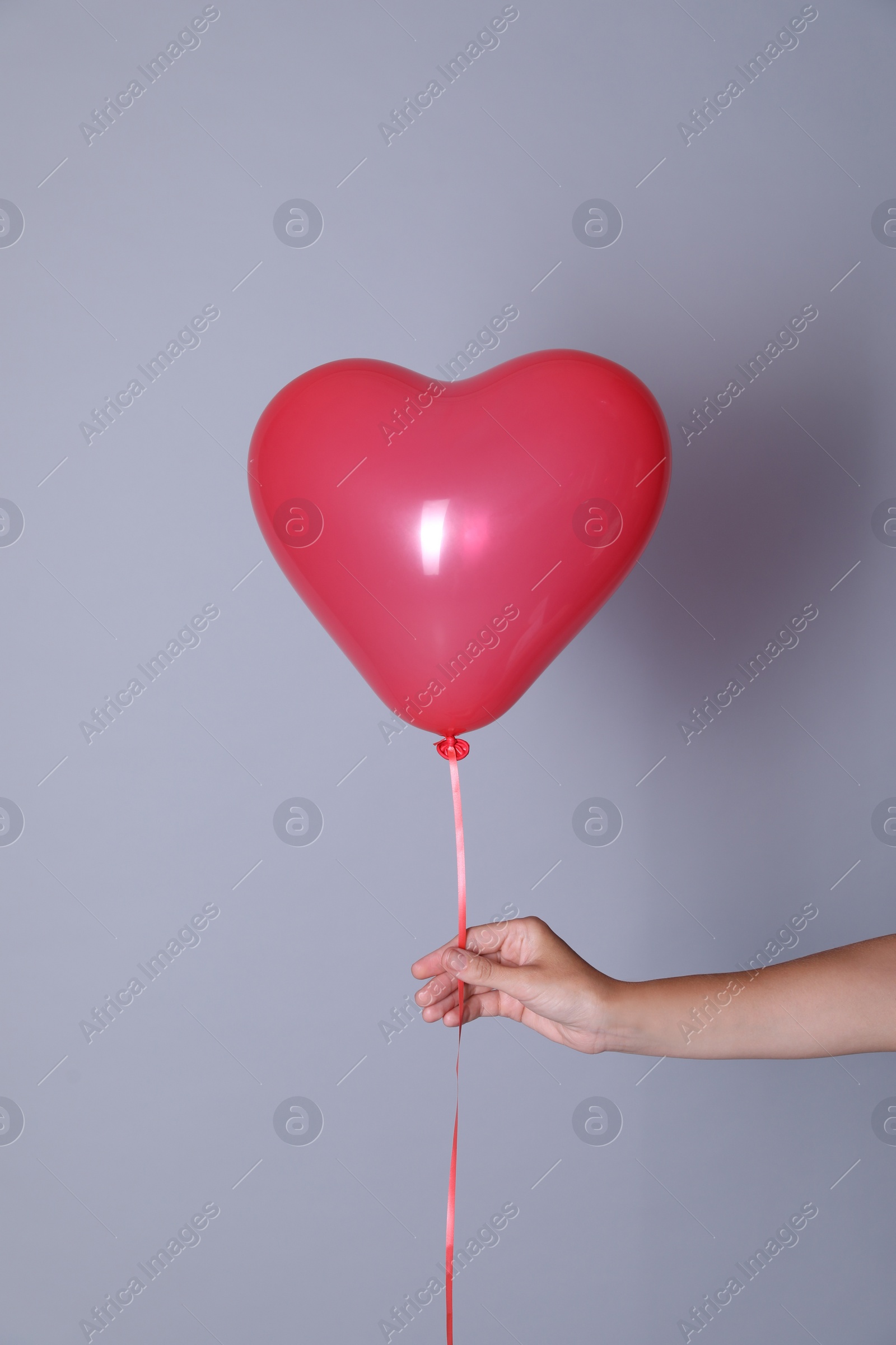 Photo of Woman holding heart shaped balloon on light background, closeup