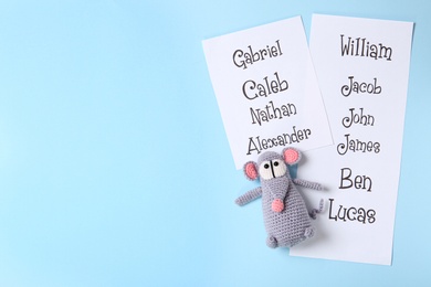 Photo of Lists of different baby names and toy on light blue background, flat lay. Space for text