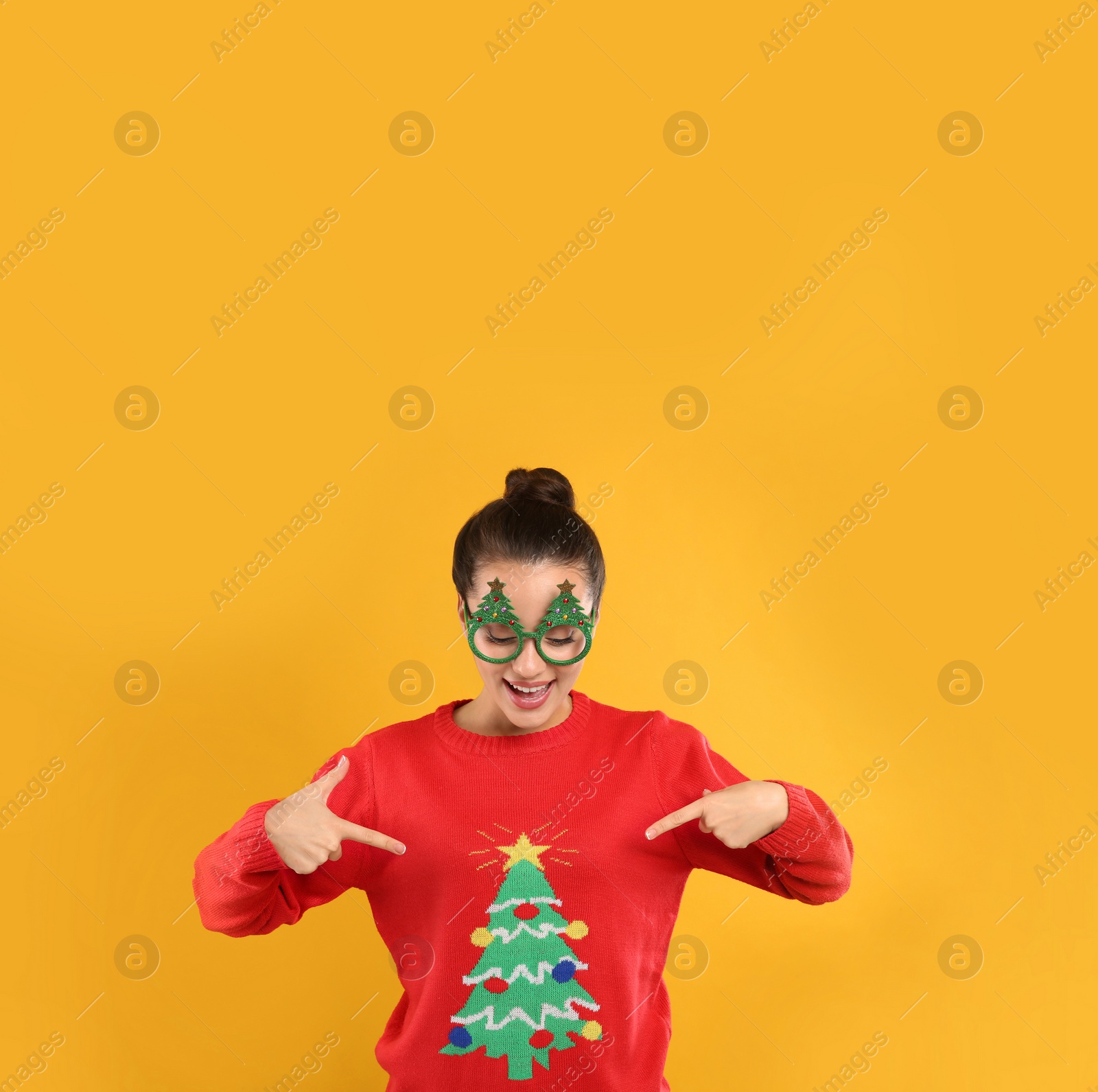 Photo of Young woman in Christmas sweater and party glasses on yellow background