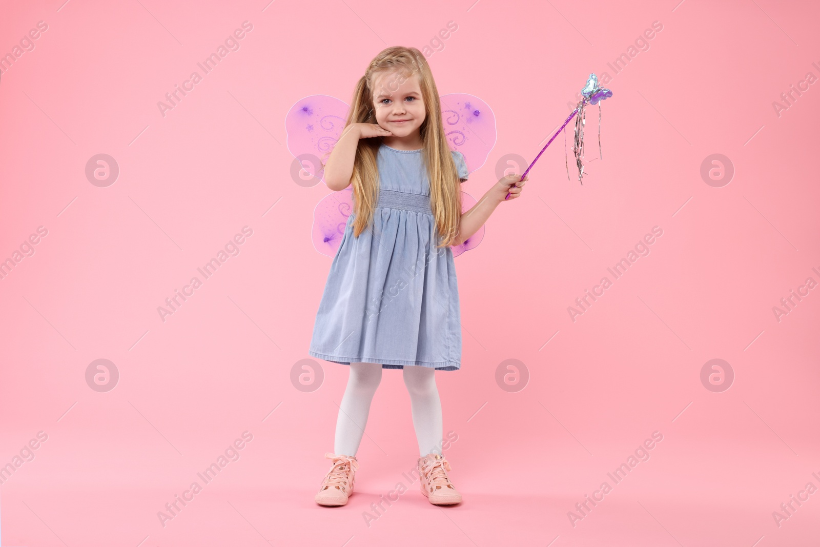 Photo of Cute little girl in fairy costume with violet wings and magic wand on pink background