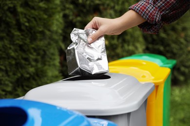 Photo of Woman throwing foil package into recycling bin outdoors, closeup