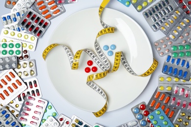 Photo of Flat lay composition with weight loss pills, plate and measuring tape on white background