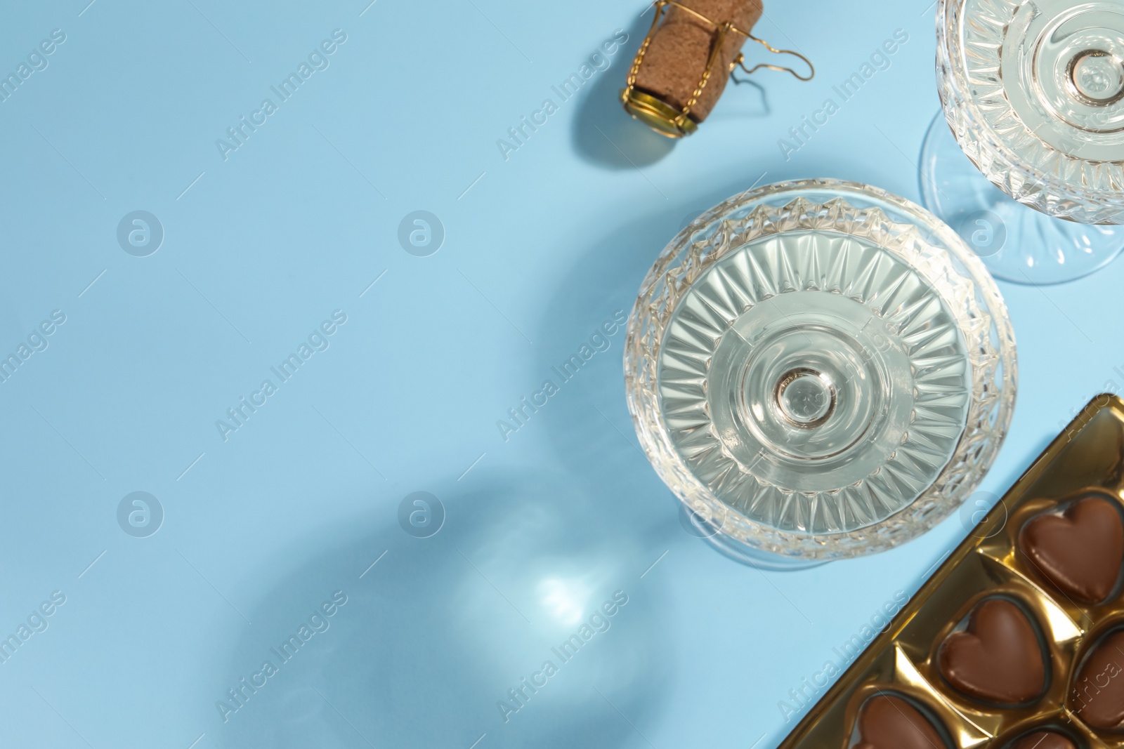 Photo of Glasses of expensive white wine, cork and heart shaped chocolate candies on light blue background, flat lay. Space for text