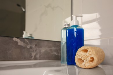 Natural loofah sponge and shower gel bottles on washbasin in bathroom, space for text