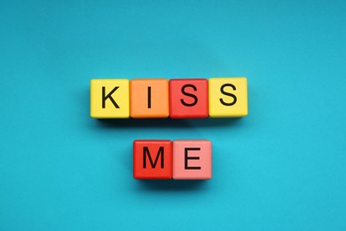 Photo of Colorful cubes with phrase Kiss Me on light blue background, flat lay