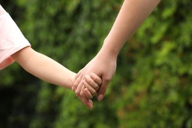 Photo of Woman and child holding hands outdoors, closeup