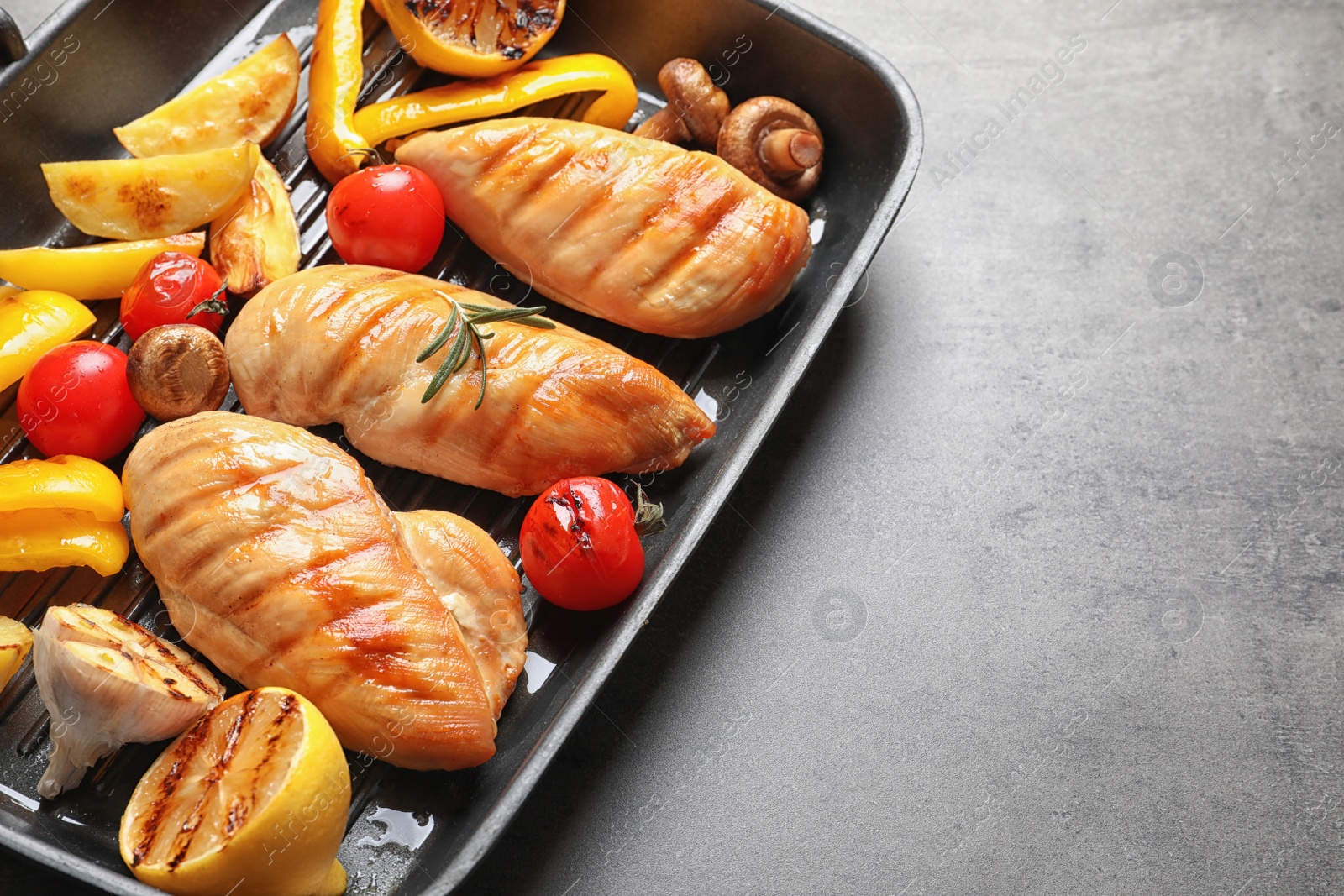 Photo of Grill pan with fried chicken breasts and garnish on grey background. Space for text