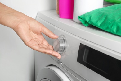 Photo of Young woman turning regulator on washing machine, closeup