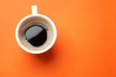 Photo of Fresh coffee in cup on orange background, top view. Space for text