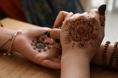 Photo of Professional mehndi master making henna tattoo at table, closeup