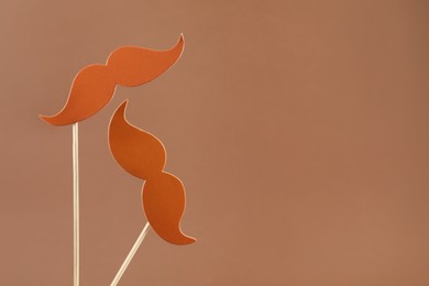 Photo of Fake paper mustaches party props on light brown background, space for text