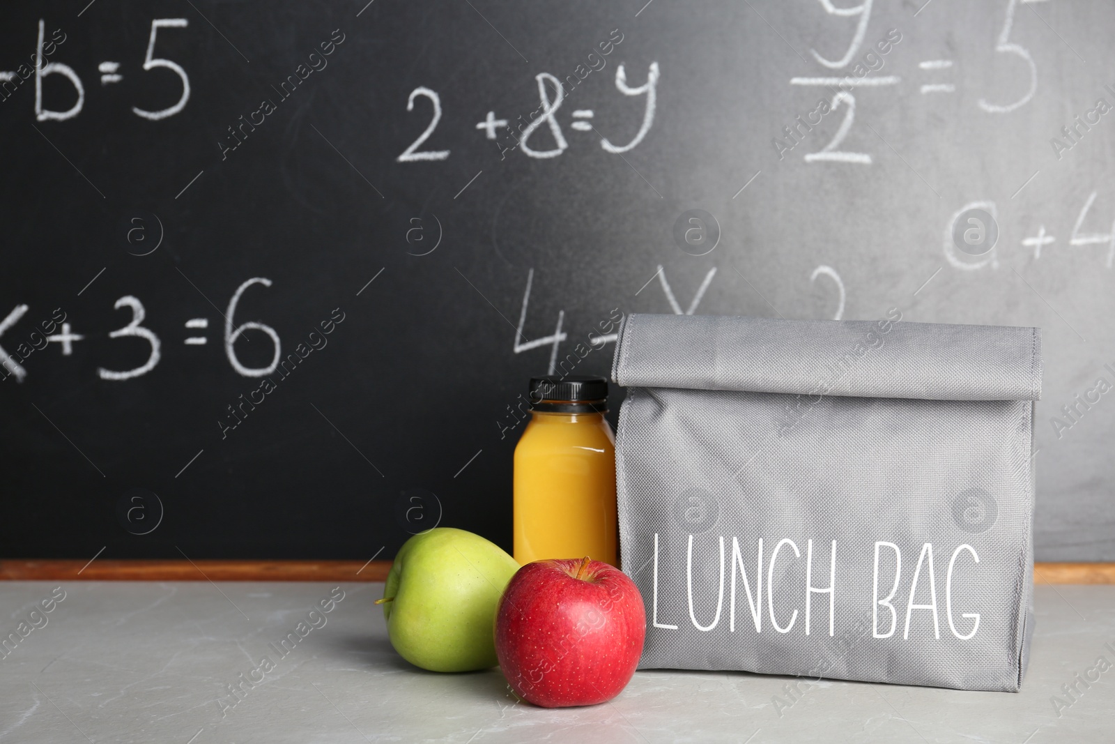Photo of Healthy food for school child in lunch bag on table near blackboard with chalk written sums