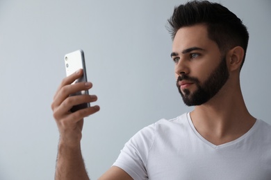 Photo of Young man unlocking smartphone with facial scanner on grey background. Biometric verification