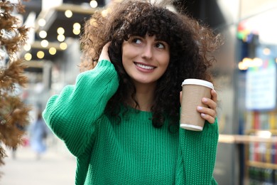 Photo of Happy young woman in stylish green sweater with cup of coffee outdoors