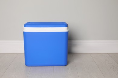 Photo of Closed blue plastic cool box near light grey wall indoors. Space for text