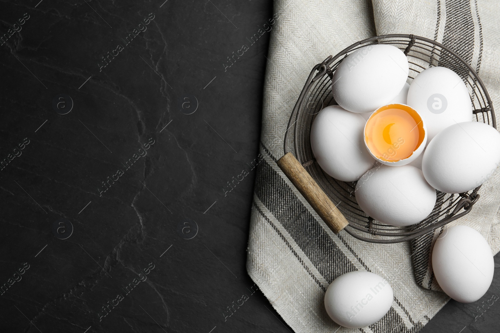 Photo of Many raw chicken eggs in metal basket on black table, flat lay. Space for text