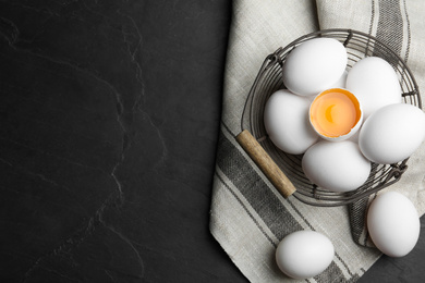 Photo of Many raw chicken eggs in metal basket on black table, flat lay. Space for text