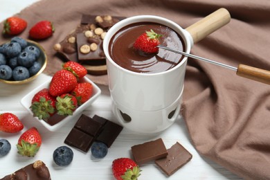 Photo of Dipping fresh strawberry in fondue pot with melted chocolate at white wooden table