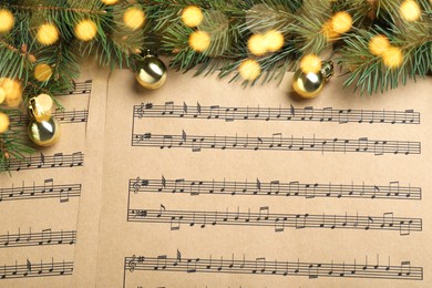 Photo of Fir branches and golden balls on Christmas music sheets, above view