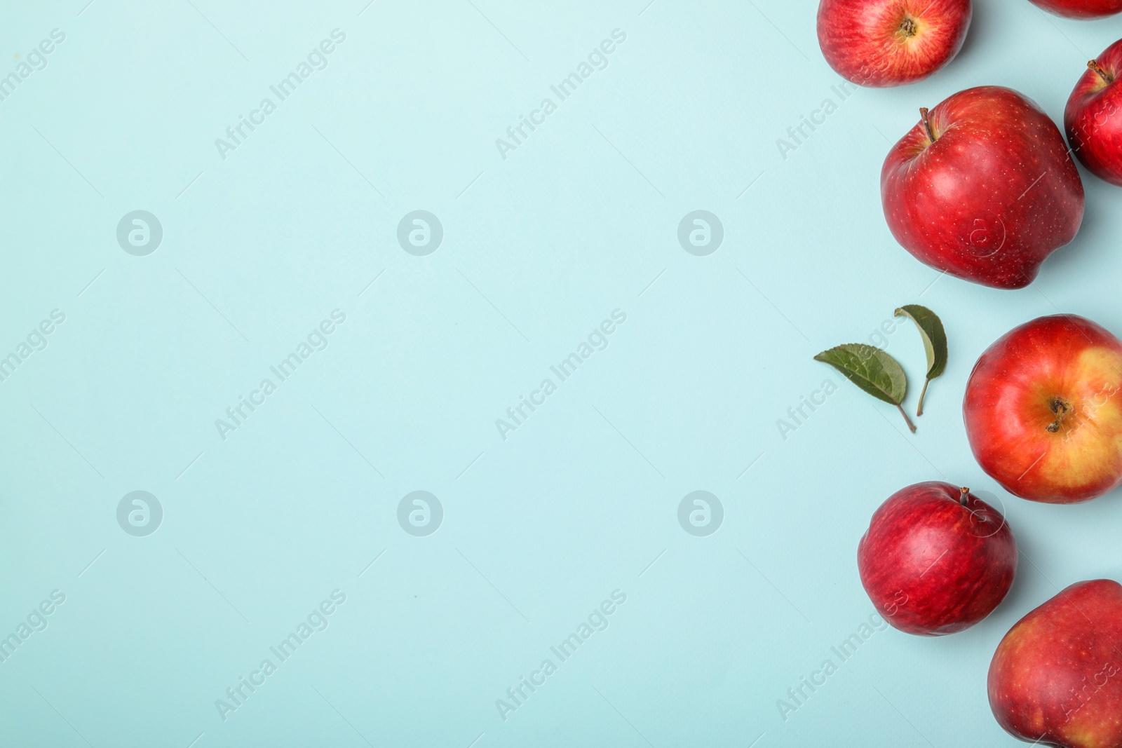 Photo of Fresh red apples and leaves on light blue background, flat lay. Space for text