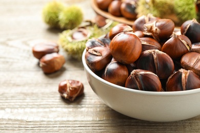 Delicious roasted edible chestnuts in bowl on wooden table, closeup