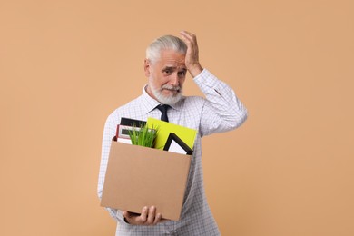 Photo of Unemployed senior man with box of personal office belongings on beige background