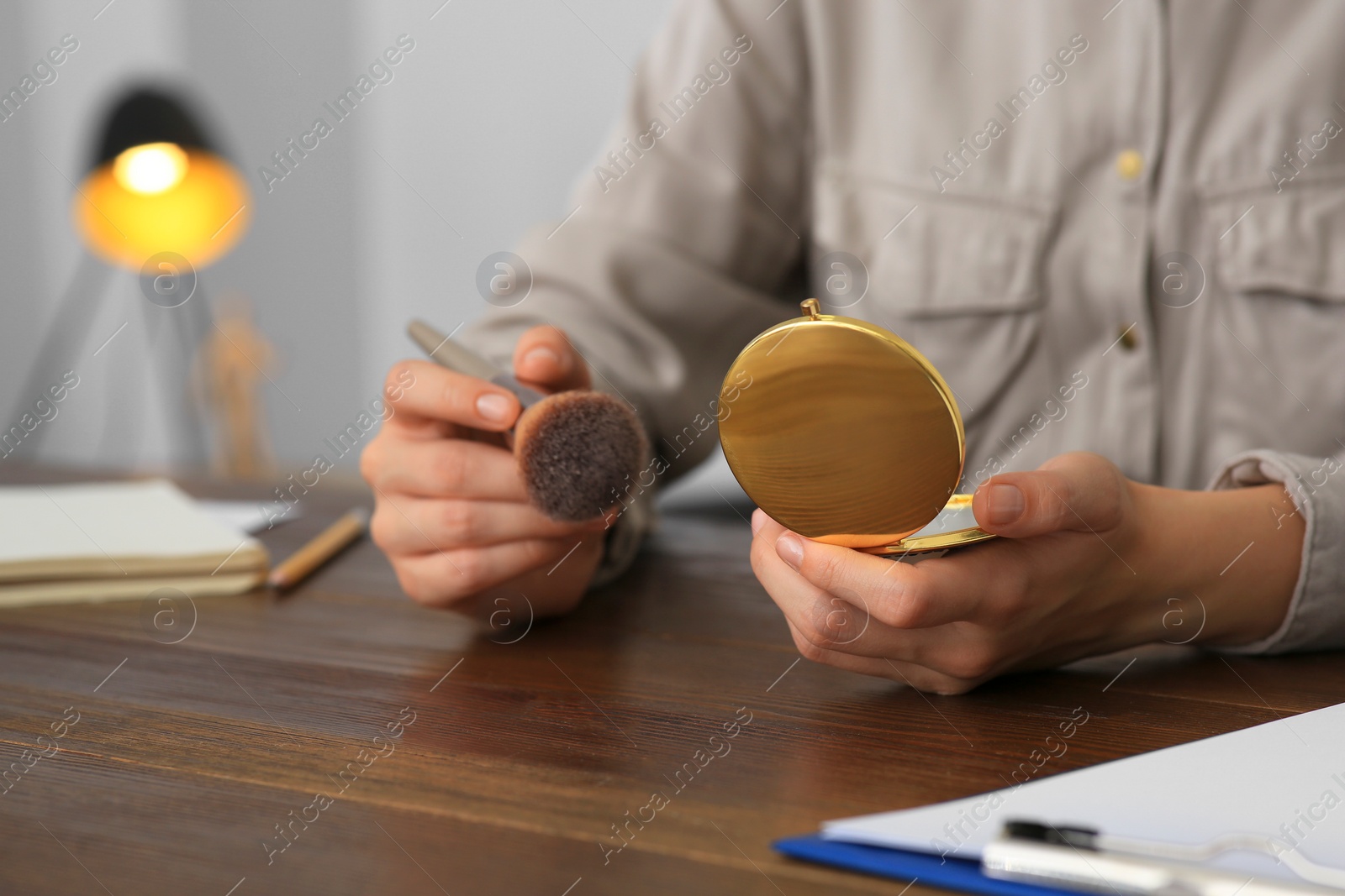 Photo of Woman with cosmetic pocket mirror and makeup brush at wooden table indoors, closeup