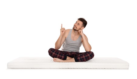 Man sitting on soft mattress and pointing upwards against white background