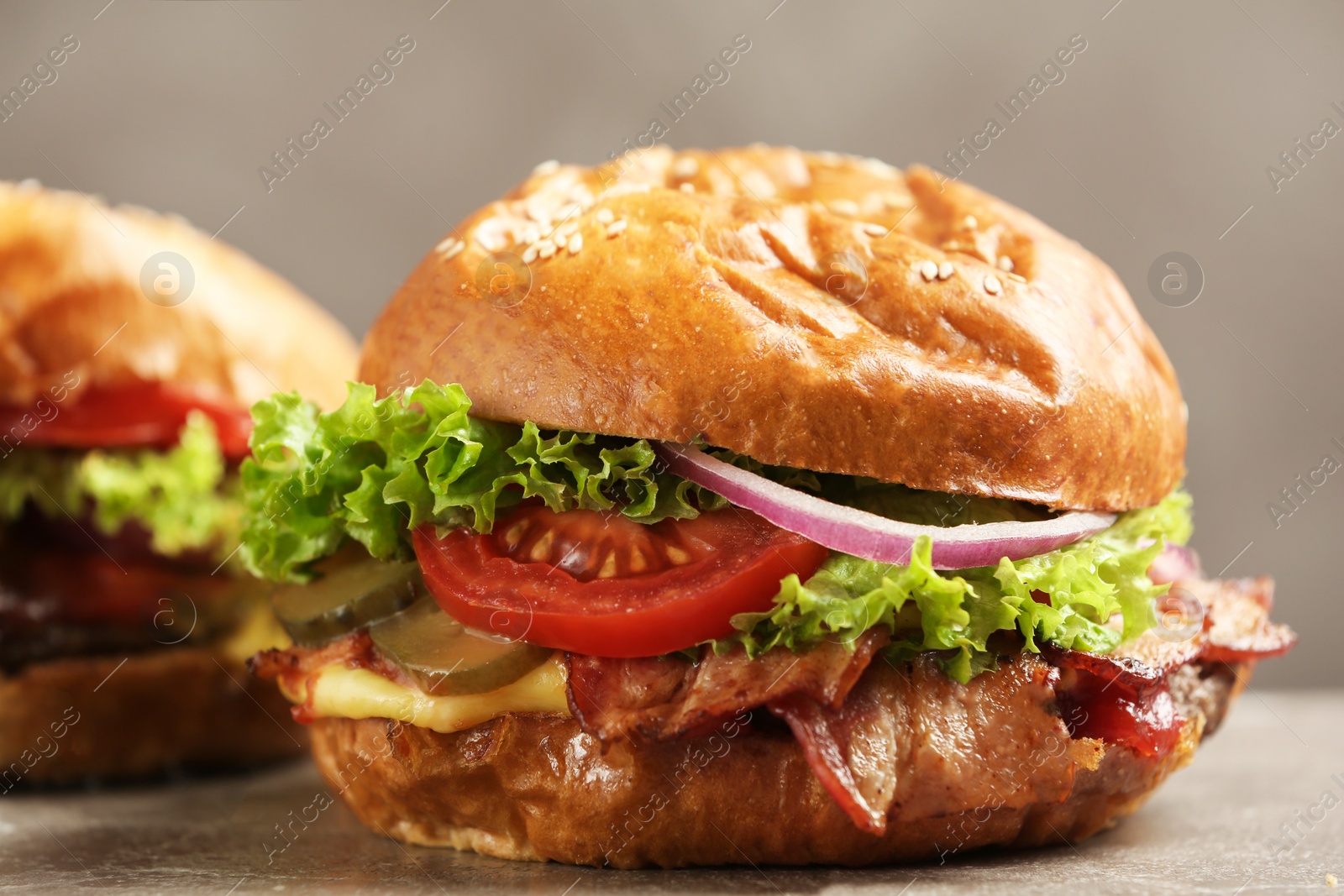 Photo of Delicious burger with bacon on table against grey background